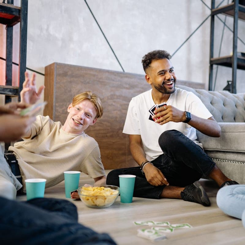 A group of friends laughing around a table during a card game - a stand-in for the Codenames, not a photograph of this model