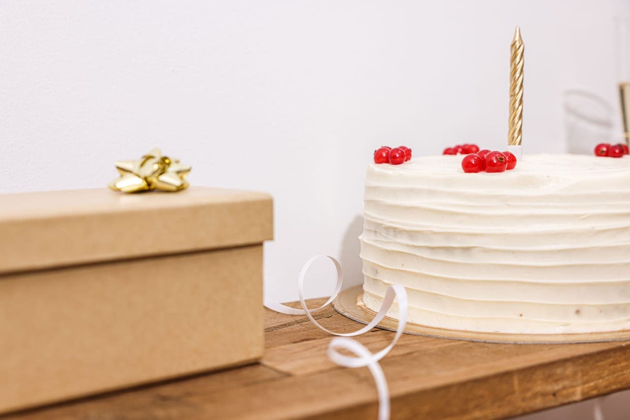 A wrapped gift box with a gold bow beside a birthday cake with a lit candle