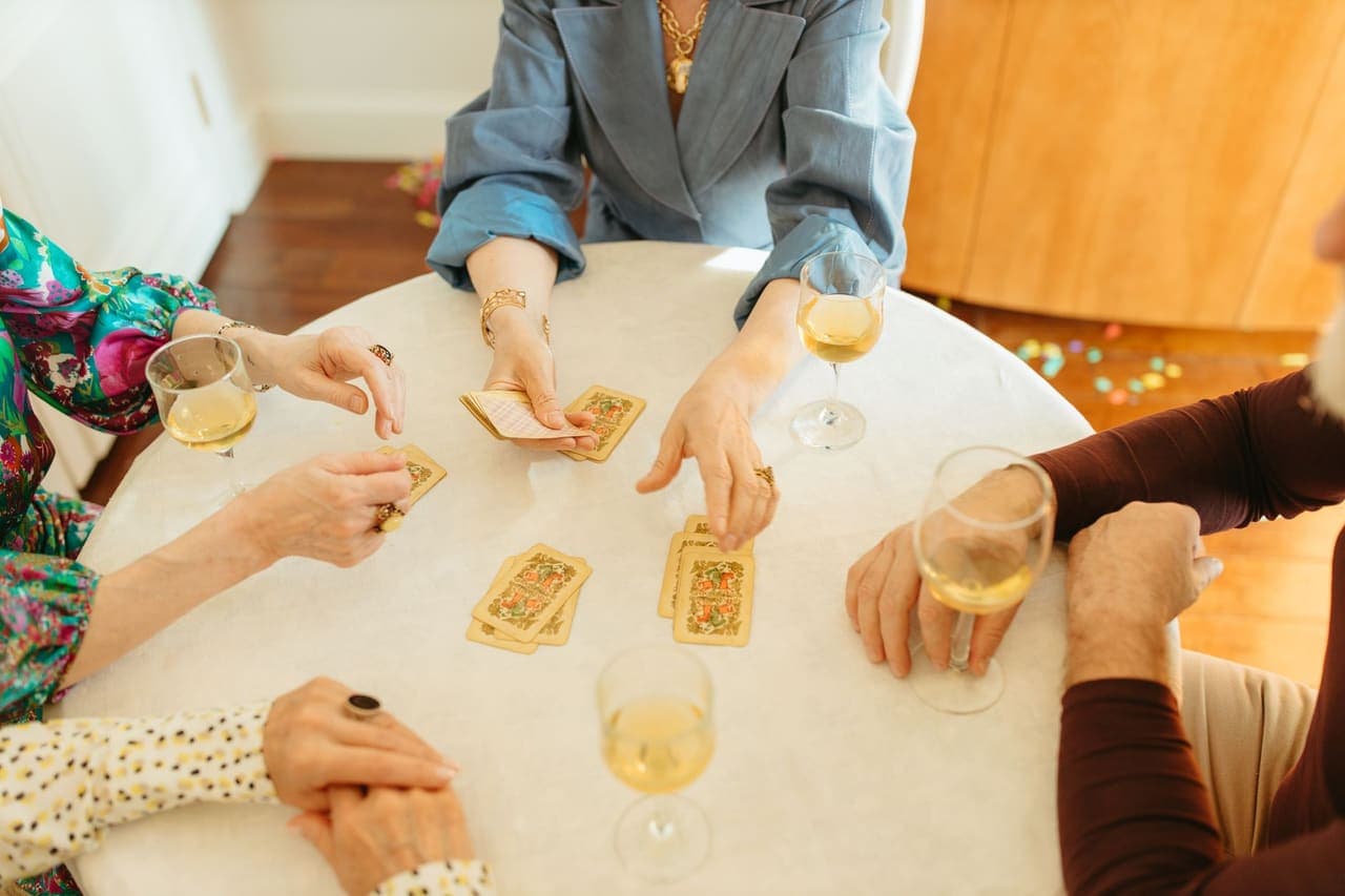 Four people playing a card game around a table with drinks