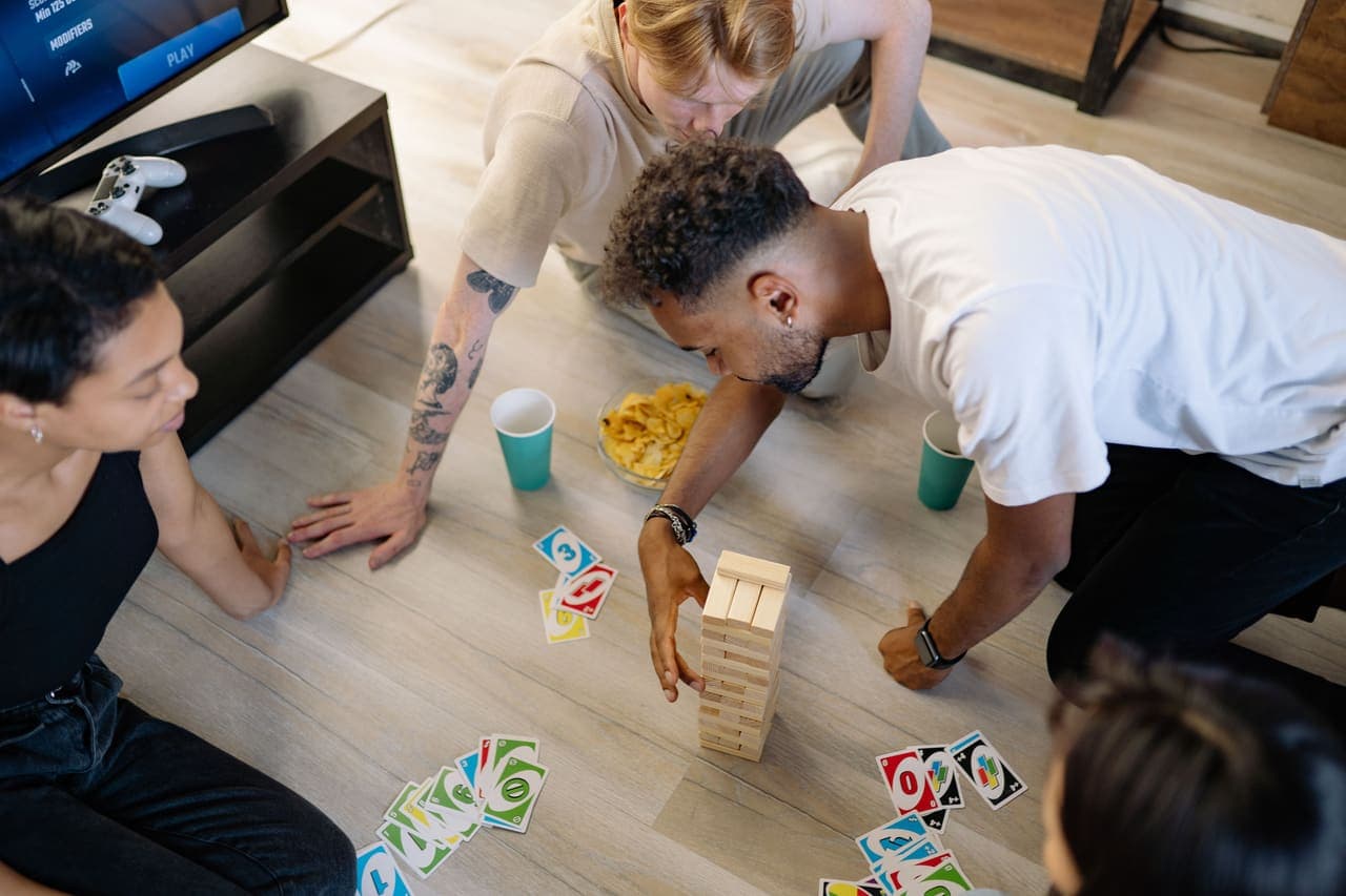 A group of friends gathered around a board game on the floor of a living room