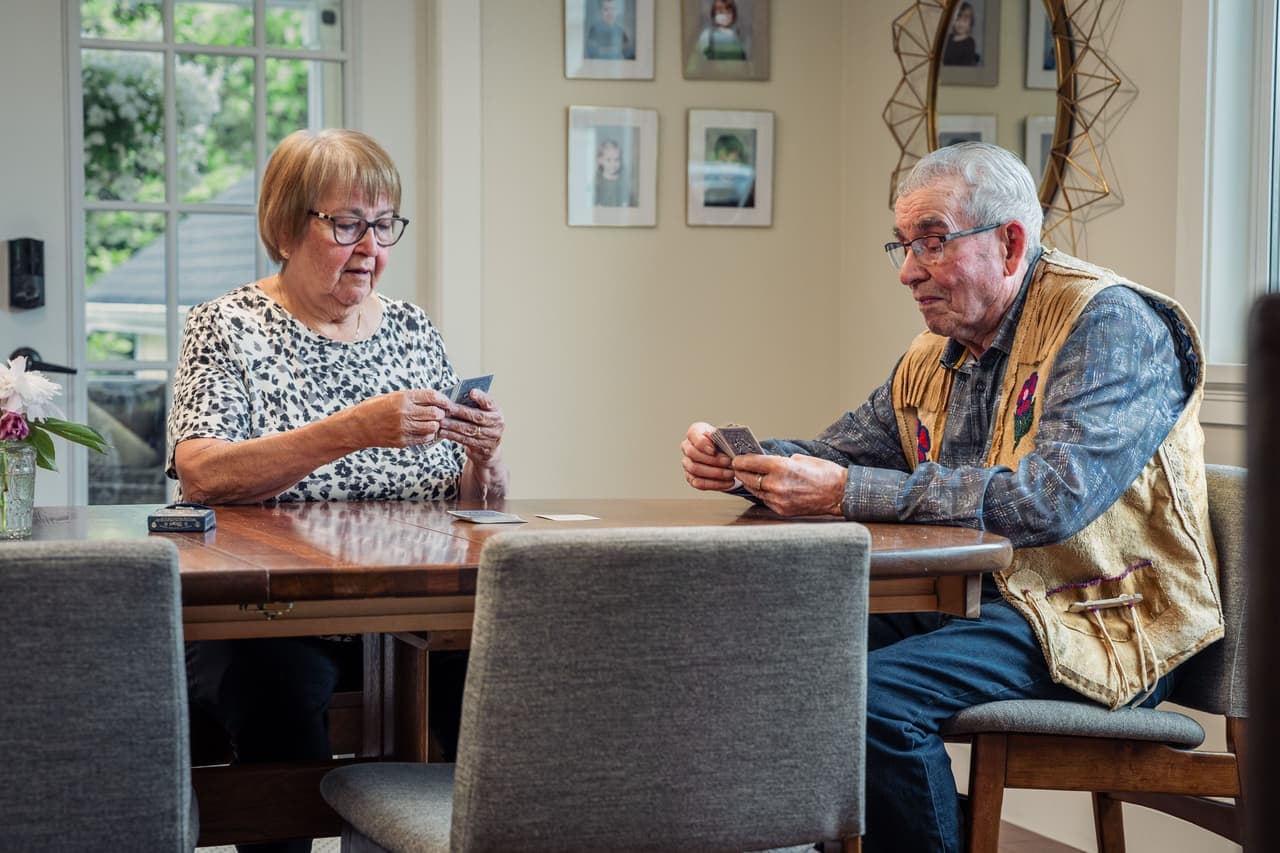 A couple playing a small card game across a kitchen table in the evening