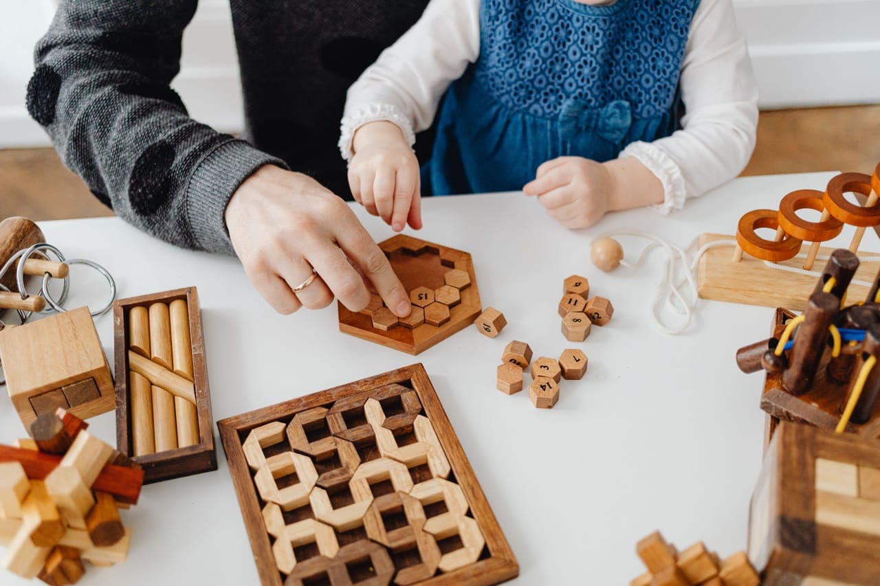 An adult and a young child playing with wooden game pieces at a table