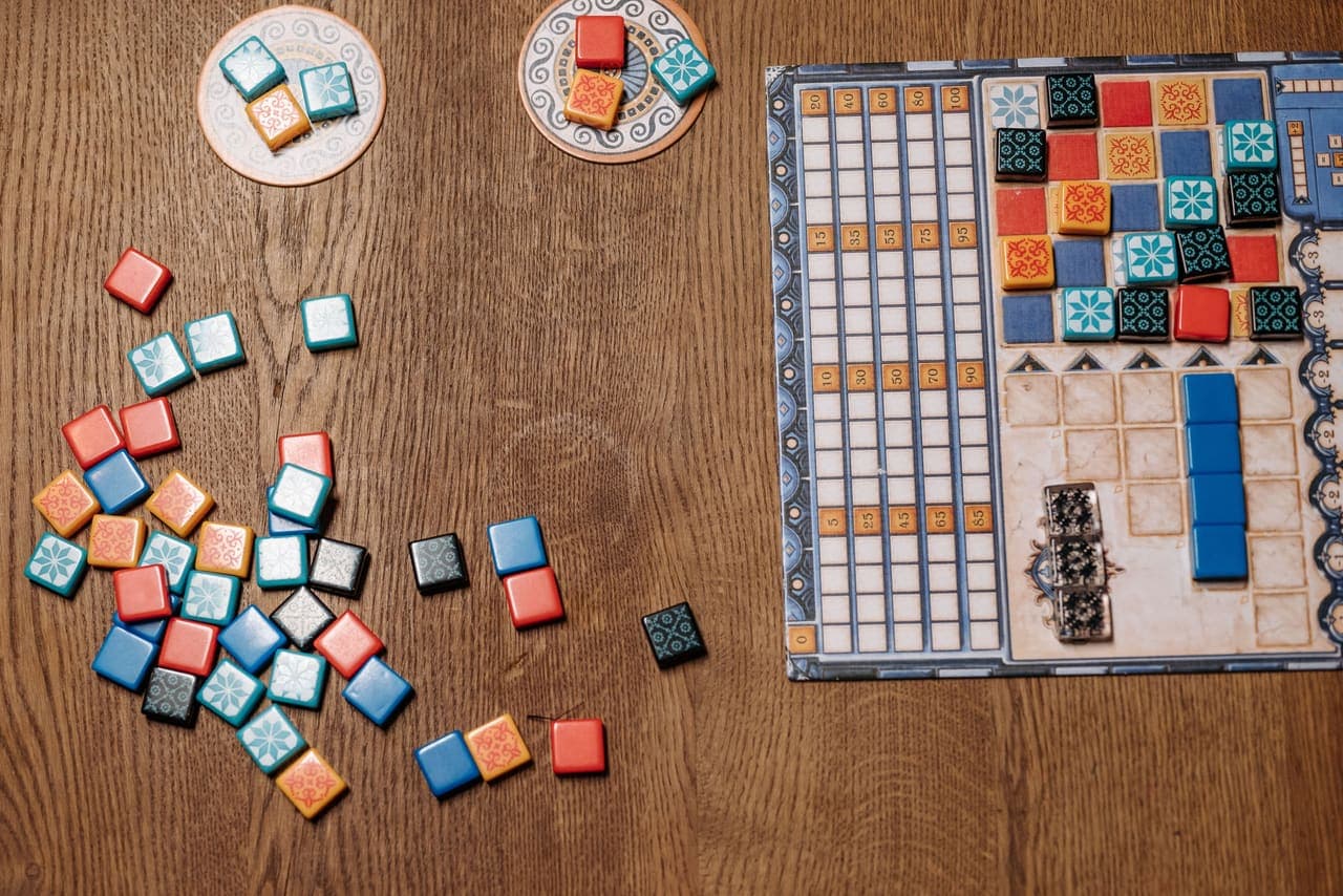 Overhead view of a tile-laying board game with colored tiles scattered on a wooden table