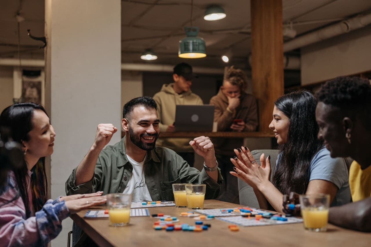 A group of friends laughing around a table covered in game components
