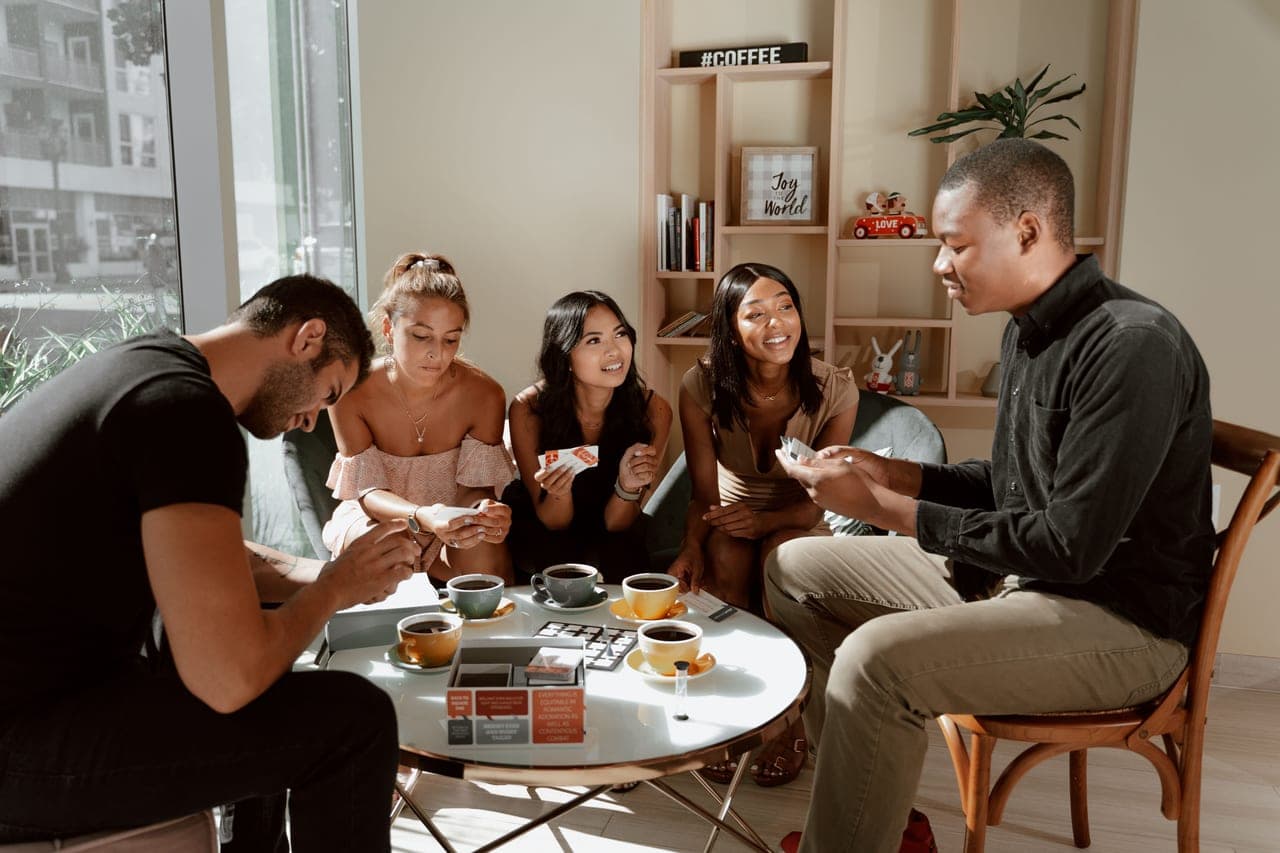 Six people crowded around a long table with a game spread across it