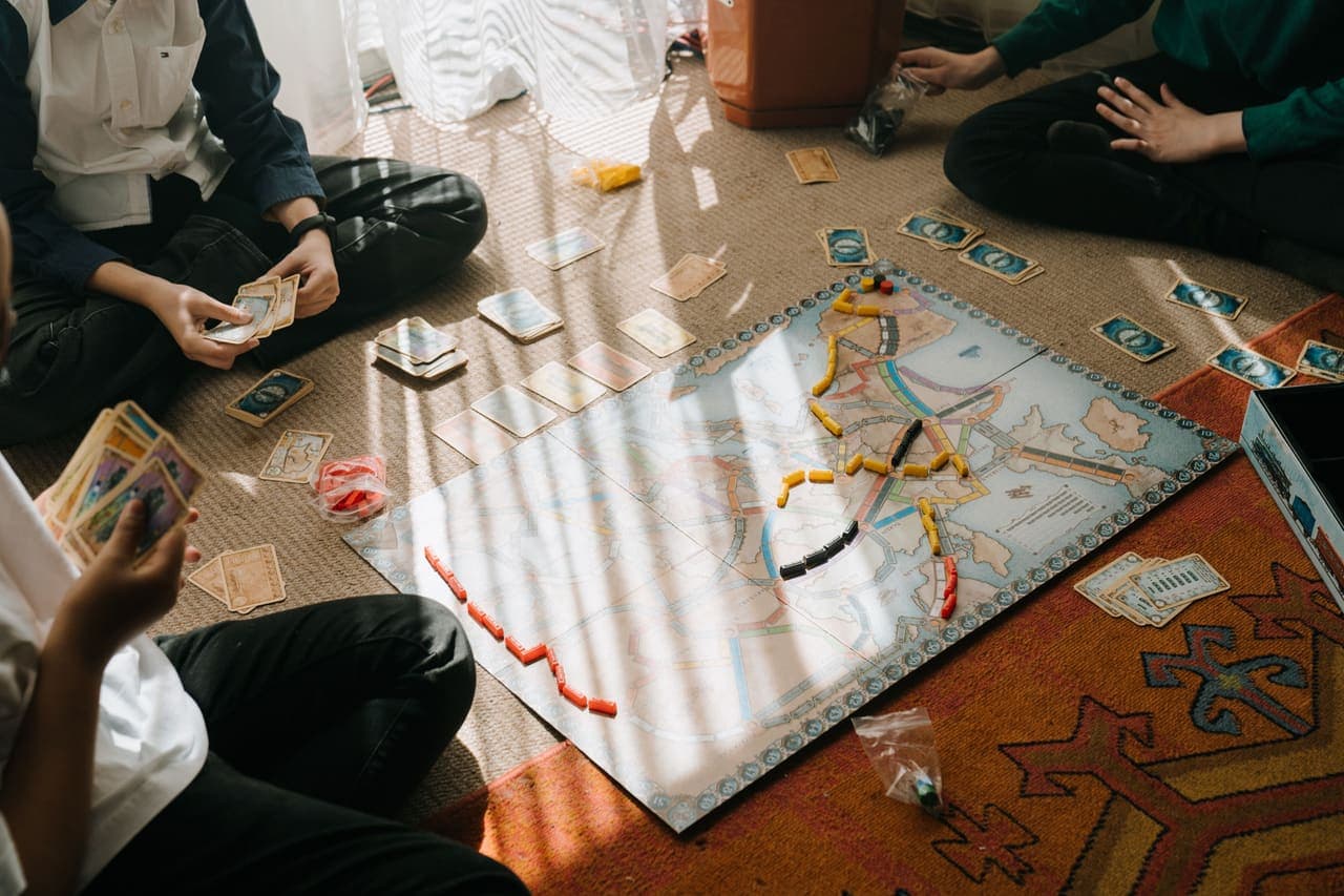 Older children sitting on the floor around a route-map board game with cards and colored pieces