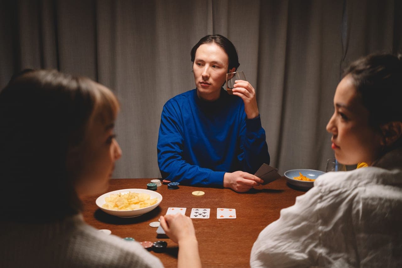 Three friends around a round table mid-game, one reaching for a card