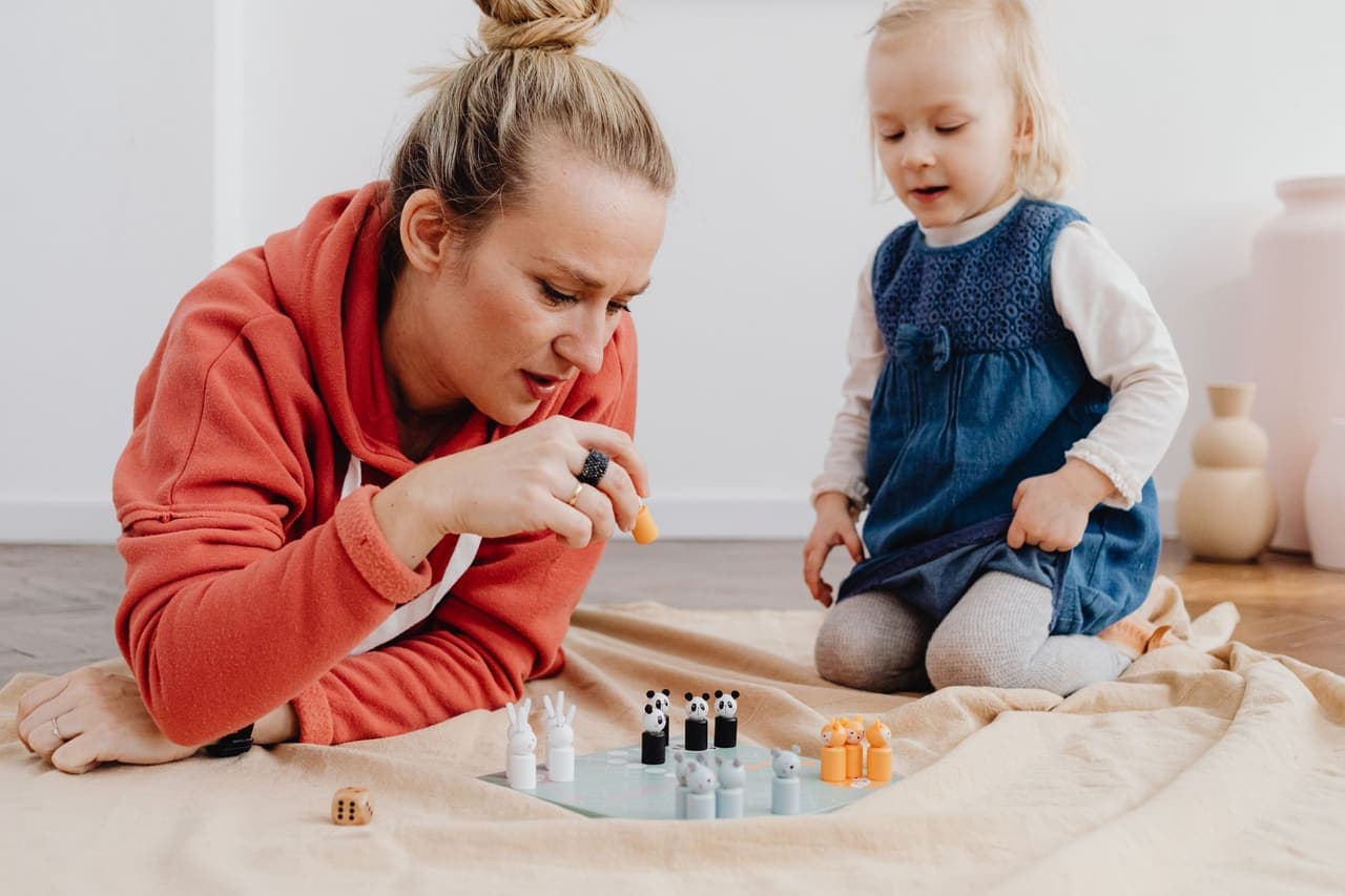 An adult and a small child kneeling on a blanket over a little board game with wooden animal pieces