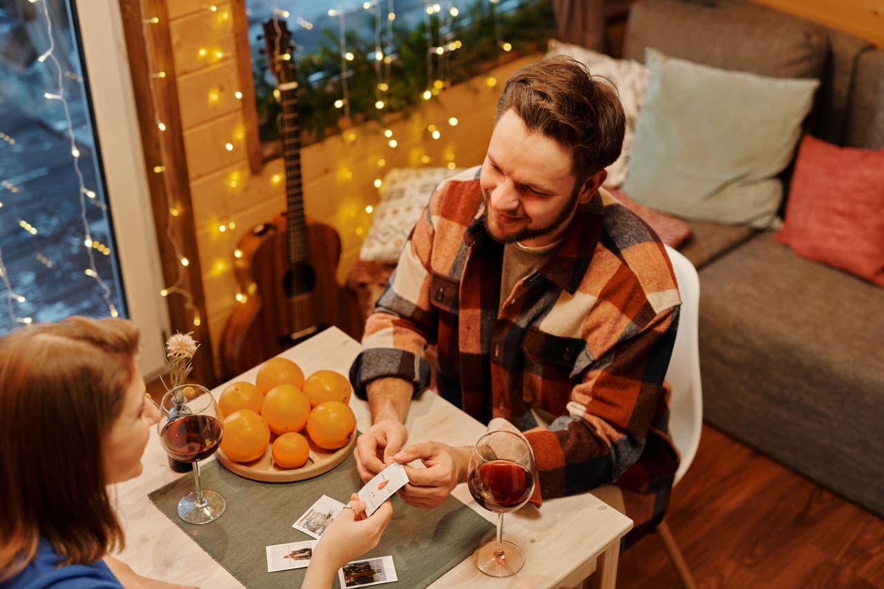 Two people playing an illustrated card game at a small table with glasses of wine