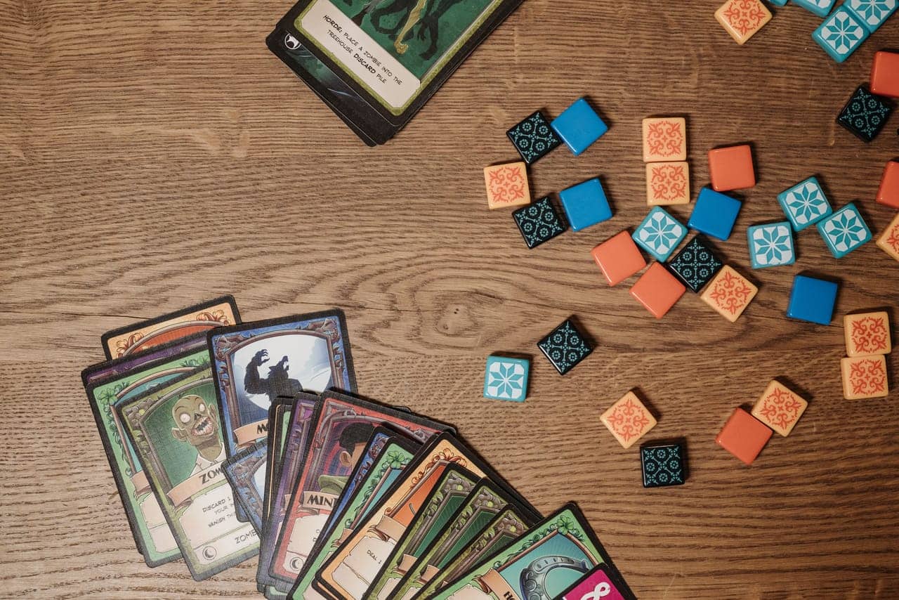 Overhead view of illustrated game cards and colored tokens spread on a wooden table