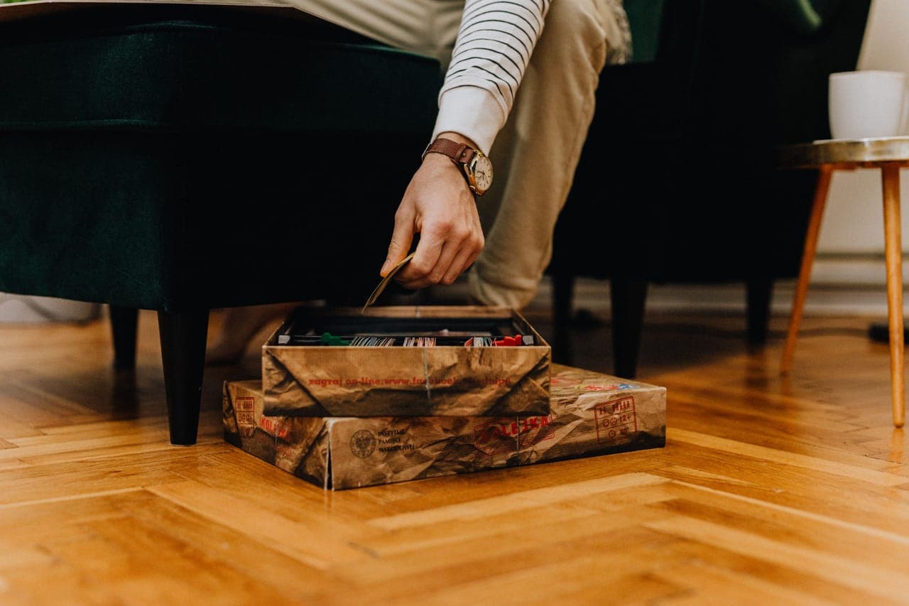 A hand reaching into an open board game box on a wooden floor