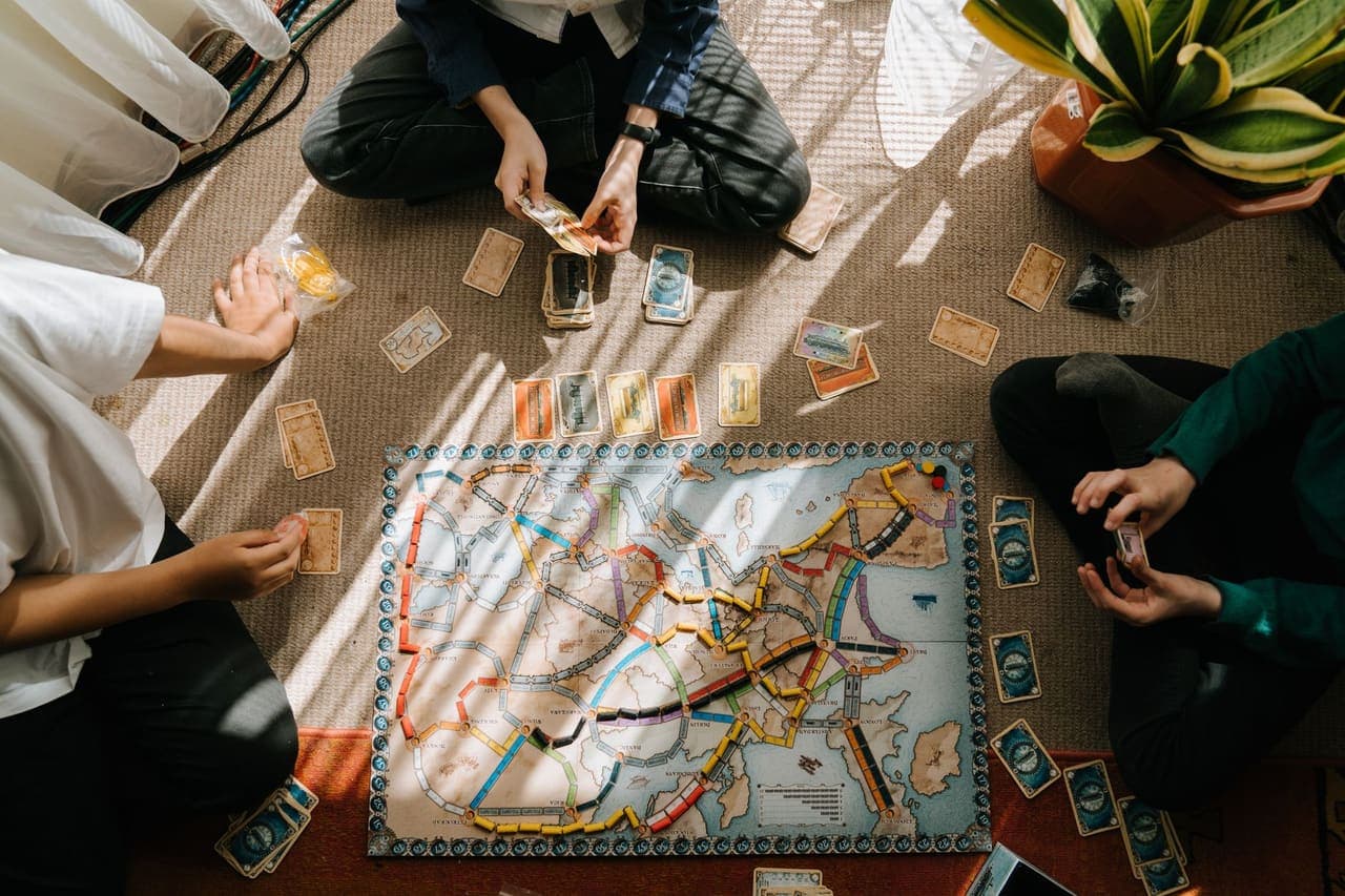 Players sitting on the floor around a route-building board game with cards spread out